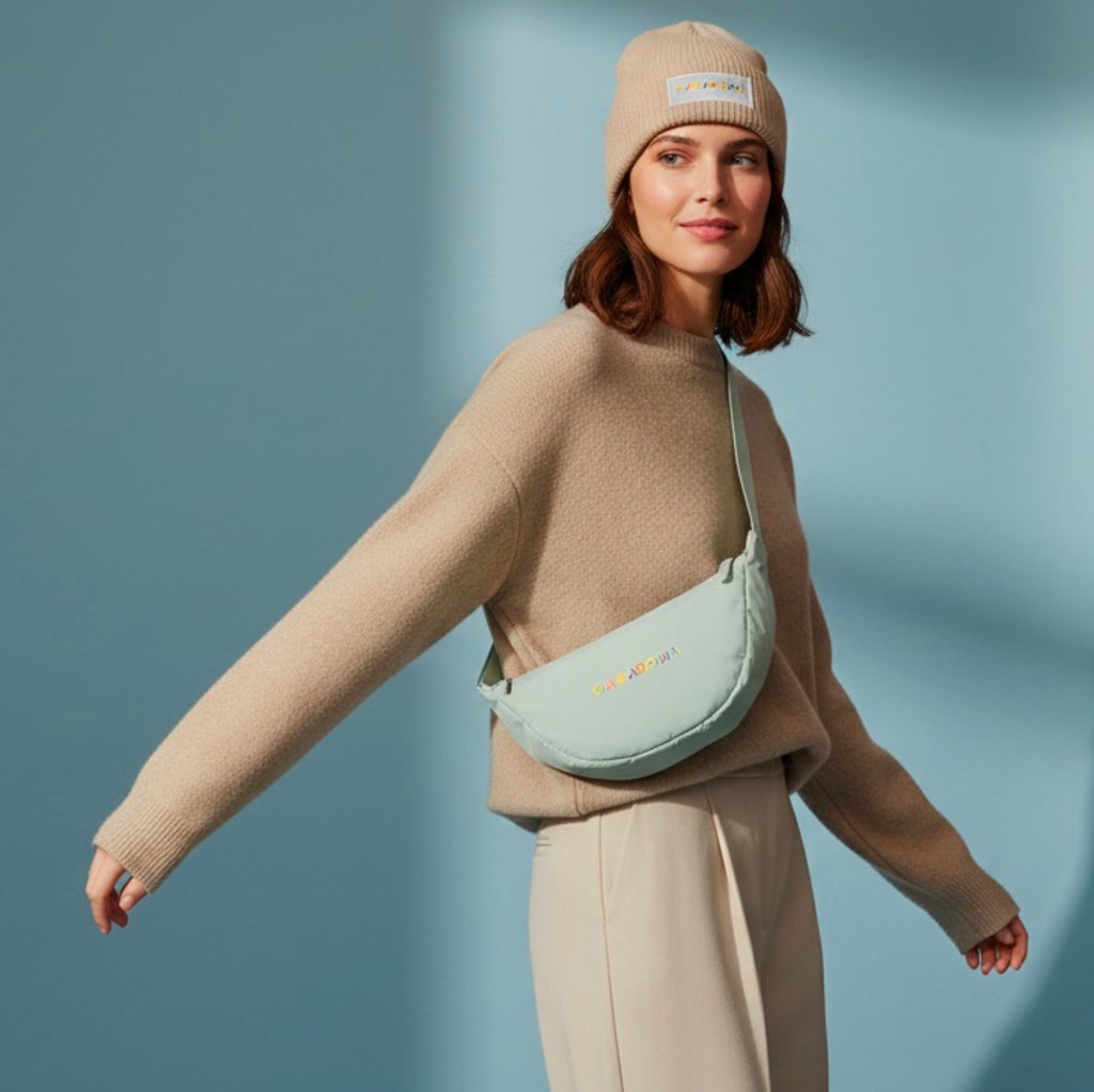 Woman wearing a beige sweater, pants, and beanie with a light green bag against a blue background